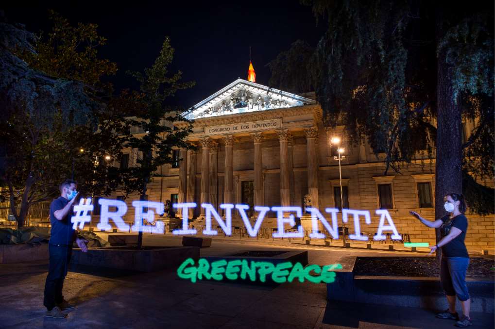 Activistas de Greenpeace despliegan frente al Congreso de los Diputados una novedosa pancarta de luz con mensajes como “Demos la vuelta al sistema” o “REinventa”.
